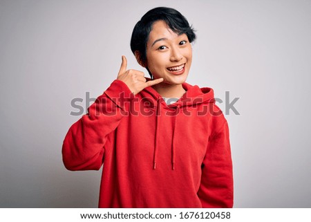 Young beautiful asian girl wearing casual sweatshirt with hoodie over white background smiling doing phone gesture with hand and fingers like talking on the telephone. Communicating concepts.