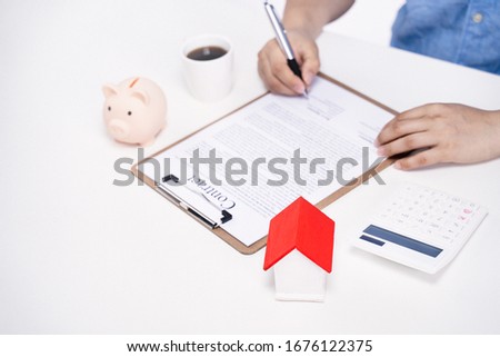 Business concept - Young Asian man in blue shirt calculates, signs agreement contract to buy a house loan payment, paying insurance, tax, close up.