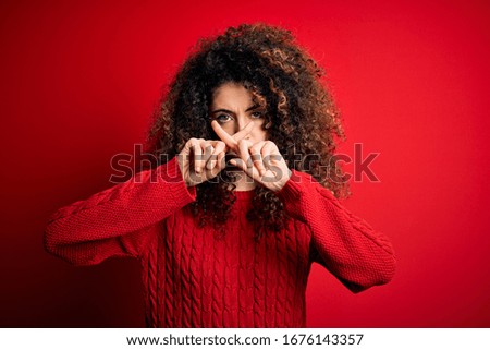 Young beautiful woman with curly hair and piercing wearing casual red sweater Rejection expression crossing fingers doing negative sign