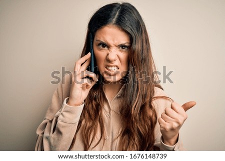 Young beautiful brunette woman having conversation talking on the smartphone annoyed and frustrated shouting with anger, crazy and yelling with raised hand, anger concept