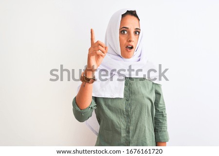 Young beautiful Arab woman wearing traditional Muslim hijab over isolated background pointing finger up with successful idea. Exited and happy. Number one.