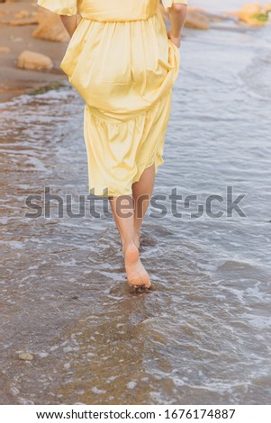 a girl in a yellow silk dress walks along the coast