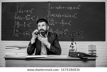 Calling parents. School teacher call mobile phone while sit classroom chalkboard background. Teacher bearded man talk mobile phone. Call colleague ask advice. Pedagogue keep in touch with colleagues.