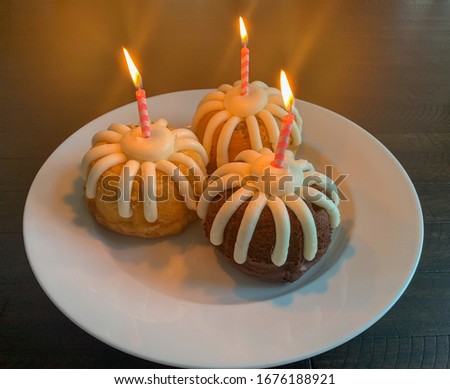 Three mini bundt cakes with frosting and pink lighted candles. 
