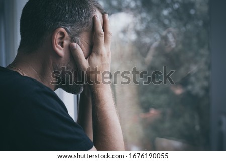 portrait one sad man standing near a window and covers his face at the day Royalty-Free Stock Photo #1676190055