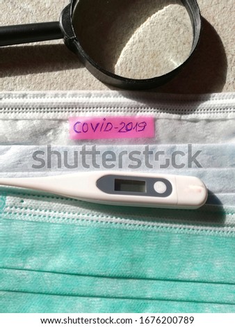 medical face mask, thermometer,magnifying glass on red paper written covid-2019