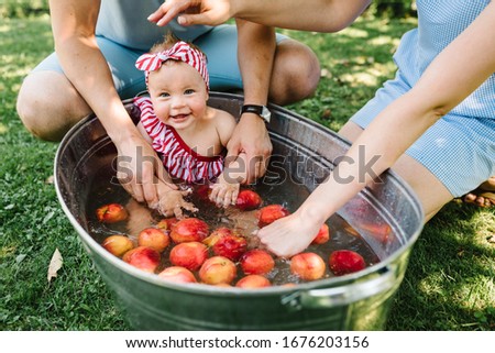 Cute little baby girl sitting in a basin on the nature and bathed in summer. Young family spending time together, outside, on vacation, outdoors. The concept of family holiday.