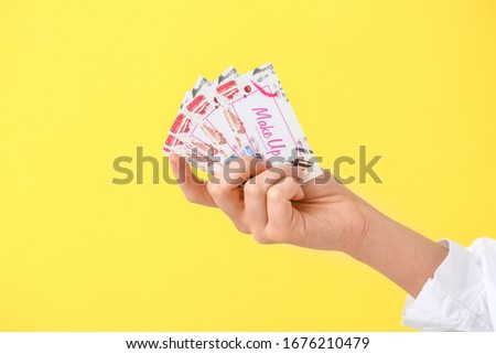 Female hand with business cards of makeup artist on color background