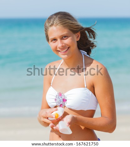 Portrait of beautiful young girl applying sunblock on a beach in summer.