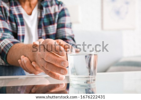 Senior man with Parkinson syndrome taking glass of water from table, closeup Royalty-Free Stock Photo #1676222431