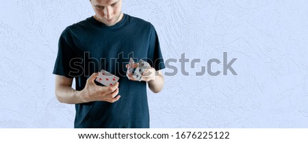 person holding some playing cards and doing the magic trick focus, standing angaist the wall wide webn banner