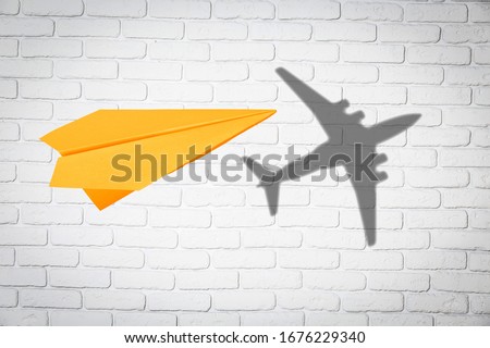 Paper plane in mid flight with a shadow of a classic real plane