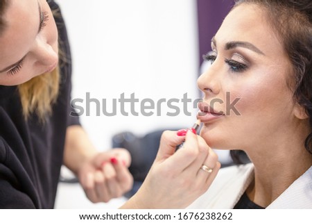 Young girl and a makeup artist make up lips