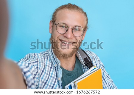 Happy young man millennial male student blogger holding smartphone looking at mobile camera record social media video blog take selfie isolated on blue background, mobile cam view, closeup portrait.