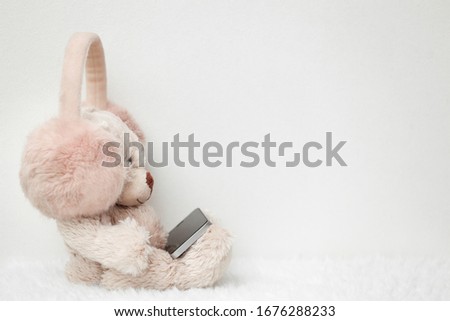 Teddy bear in pink headphones with smartphone on a white background