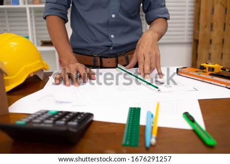 Architect using calculator Estimate construction drawings with blueprint in construction site.