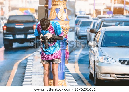A young photographer in wet clothes use DSLR camera to take pictures of Songkran water splashing festival on the road in the city.