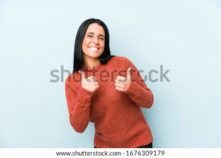 Young caucasian woman isolated on a blue background raising both thumbs up, smiling and confident.