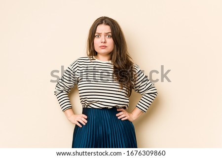 Young curvy woman shrugs shoulders and open eyes confused.
