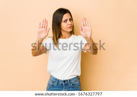 Young woman isolated on beige background standing with outstretched hand showing stop sign, preventing you.