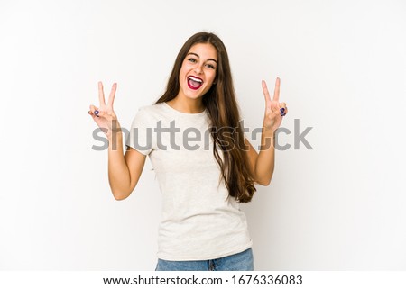 Young caucasian woman isolated on white background showing victory sign and smiling broadly.
