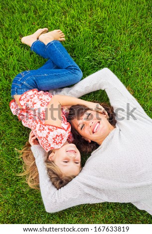 Happy mother and daughter relaxing outside on green grass. Spending quality time together, Real emotions