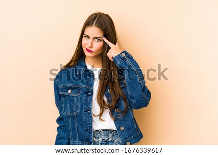 Young caucasian woman isolated en beige background pointing temple with finger, thinking, focused on a task.