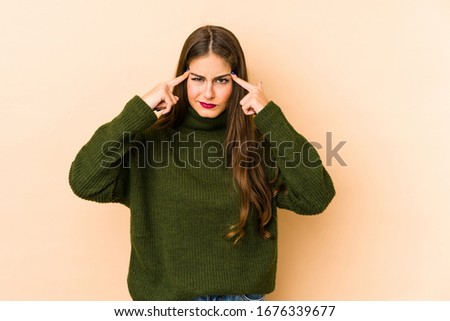 Young caucasian woman isolated en beige background focused on a task, keeping forefingers pointing head.