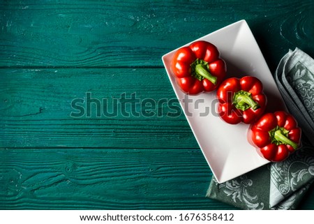 Red bell pepper on a white plate on a dark green wooden background with a vintage napkin