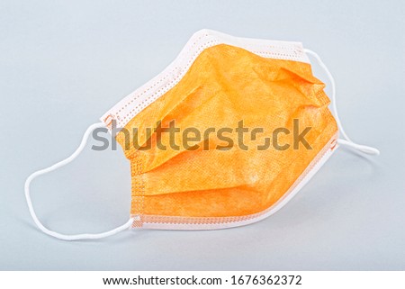 Close up of orange disposable face mask on grey background. Protective face mask.
