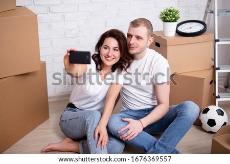 moving day - portrait of happy young couple taking selfie photo with cardboard boxes in their new house or flat