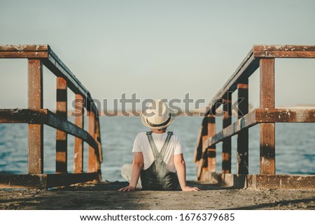 Back view of a Pensive child sitting looking at the sea outdoor
