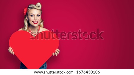 Woman holding paper heart shape. Pin up girl. Retro fashion and vintage. Red color background. Copy space for some text. Valentine or Like symbol. Wide horizontal banner composition.