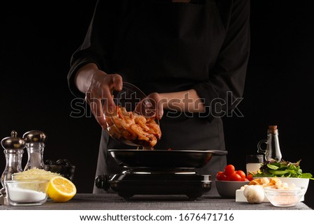 Chef cooks shrimps for salad, frying in a skillet. Sea food and cooking. Peppers. Delicious and healthy food on a black background. Cooking and gastronomy, a bunch of recipes.