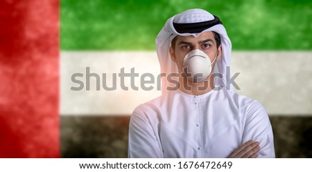 Emirati young man wearing medical mask to protect himself from coronavirus standing front UAE flag background Royalty-Free Stock Photo #1676472649
