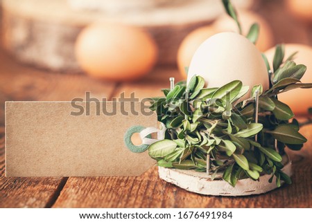 Natural eggs in basket from bunch plant and empty tag for text on wooden table in sunny morning. Eco-friendly Easter concept.