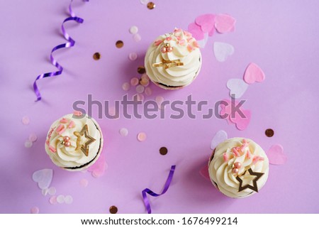 Cupcakes Dessert, Confetti and Festive Ribbons Top View Copy Space Photography. Muffins with Rose Chocolate Chips, Elegance Sweet Balls and Golden Star. Purple Background Flat Lay Photo