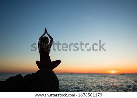 Silhouette of woman practicing yoga during soft amazing sunset on ocean beach. 