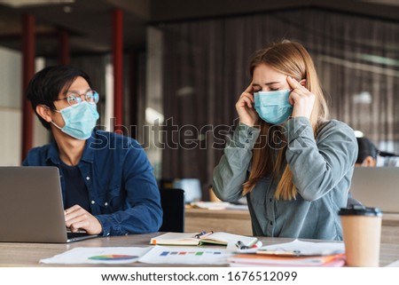 Photo of multinational young students with headache in medical masks studying on laptop at classroom