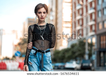 Young stylish woman standing outdoors blurred urban background posing to camera confident