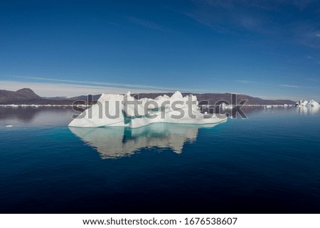 Iceberg in Greenland fjord with reflection in calm water. Sunny weather. Golden hour.
