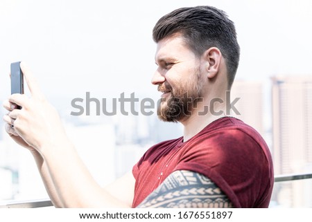 Profile of a young man with beard in summer clothes making a selfie outside with a city in the background in Kuala Lumpur in Malaysia