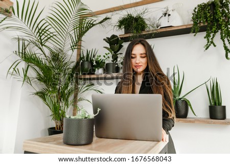 Attractive businesswoman with dark hair, wears a black jacket, works on a laptop in a cozy cafe, looks at the screen with a smile on her face.Businesswoman freelancer uses a laptop in a hipster cafe