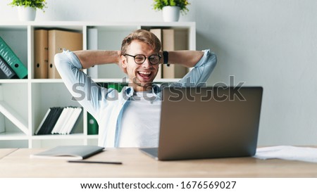 Young man smiling as he reads the screen of a laptop computer while relaxing working on a comfortable place by the wooden table at home. Happy Social distancing Royalty-Free Stock Photo #1676569027