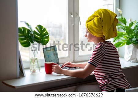 Woman with yellow towel on head is working office work remotely from home on bed. Using computer. Distance learning online education and work Royalty-Free Stock Photo #1676576629