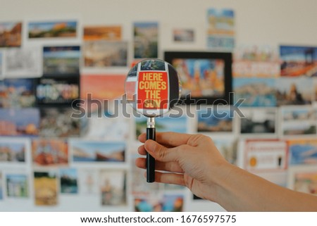 Hand holding magnifier focusing on "here comes the sun" poster on wall