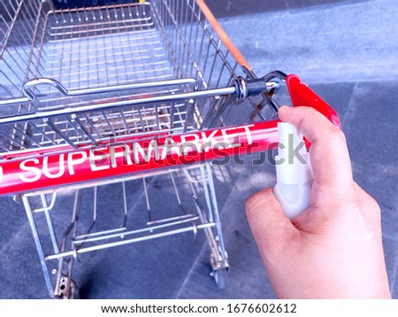Cleaning shopping cart holder with alcohol spray. Corona Virus or bacteria infected protection from touch public object. Customer self-protection in public place concept. Royalty-Free Stock Photo #1676602612