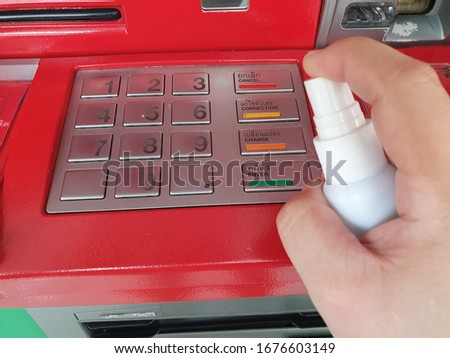 Cleaning switch button of ATM (Automatic teller machine) before withdrawing cash or financial transaction with alcohol spray. Corona Virus or bacteria infected protection from touch public object.  Royalty-Free Stock Photo #1676603149
