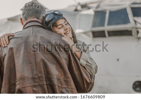 Waist up of happy kid wearing aviator hat while embracing his father outdoors stock photo