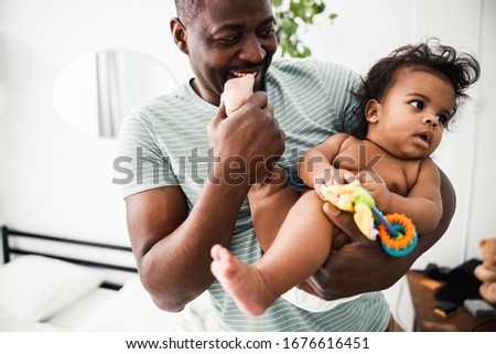 Cheerful father holding adorable baby girl and biting her tiny foot stock photo